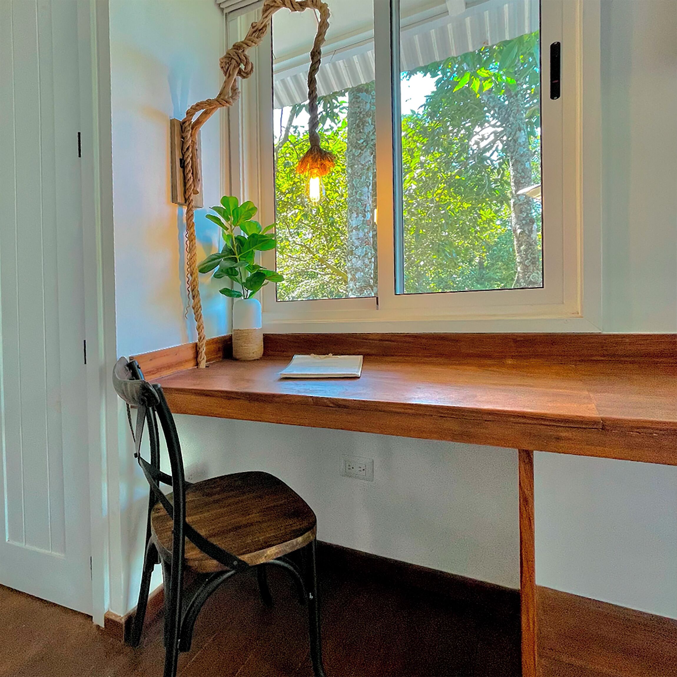 A corner desk with a plant, a lamp, and a window with a view of trees.