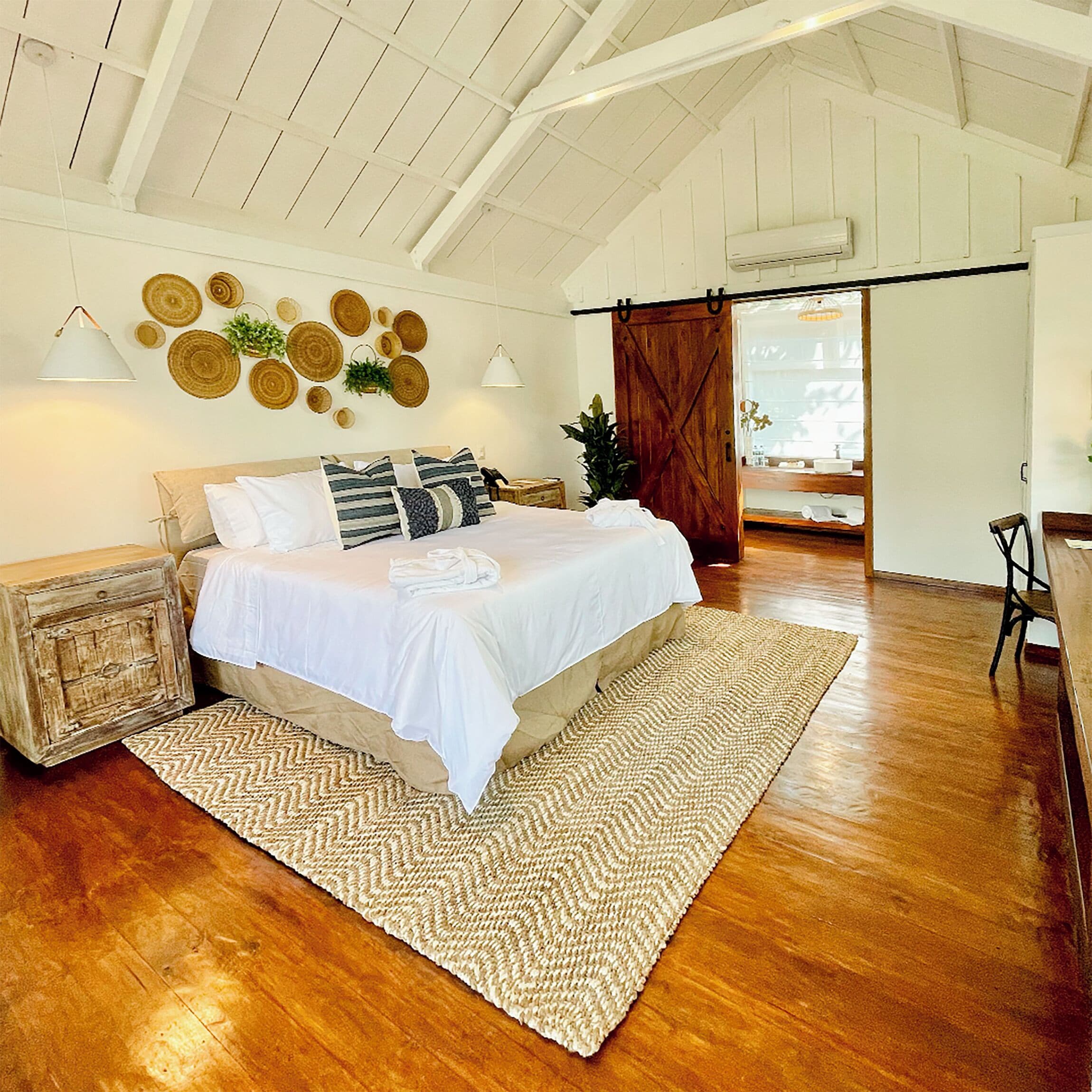 A spacious bedroom with a large bed, wooden flooring, and a rustic ceiling.