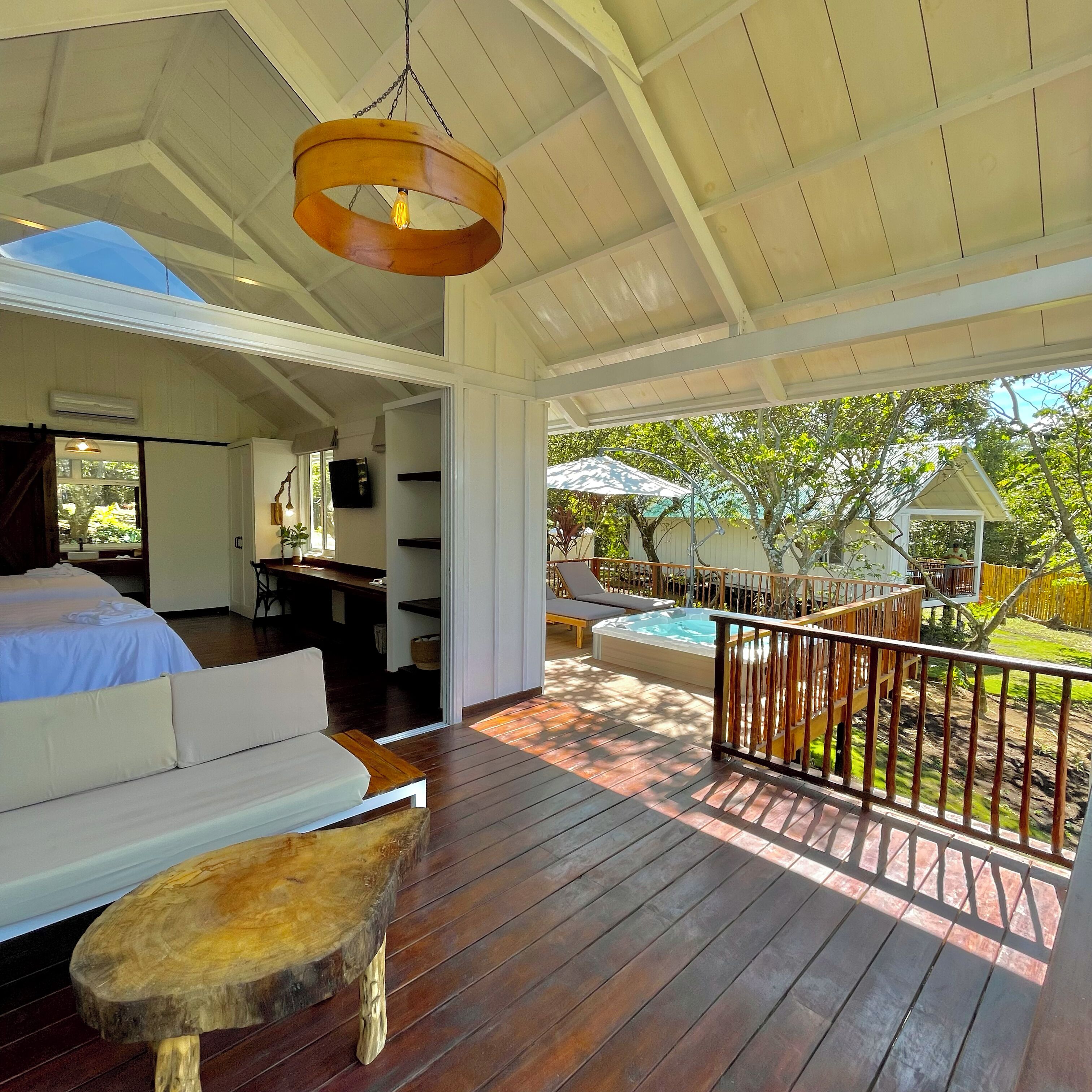 Un espacio exterior amplio con terraza de madera, un jacuzzi y una zona de estar con sofá y taburete de madera.