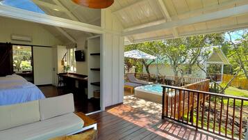 Un espacio exterior amplio con terraza de madera, un jacuzzi y una zona de estar con sofá y taburete de madera.