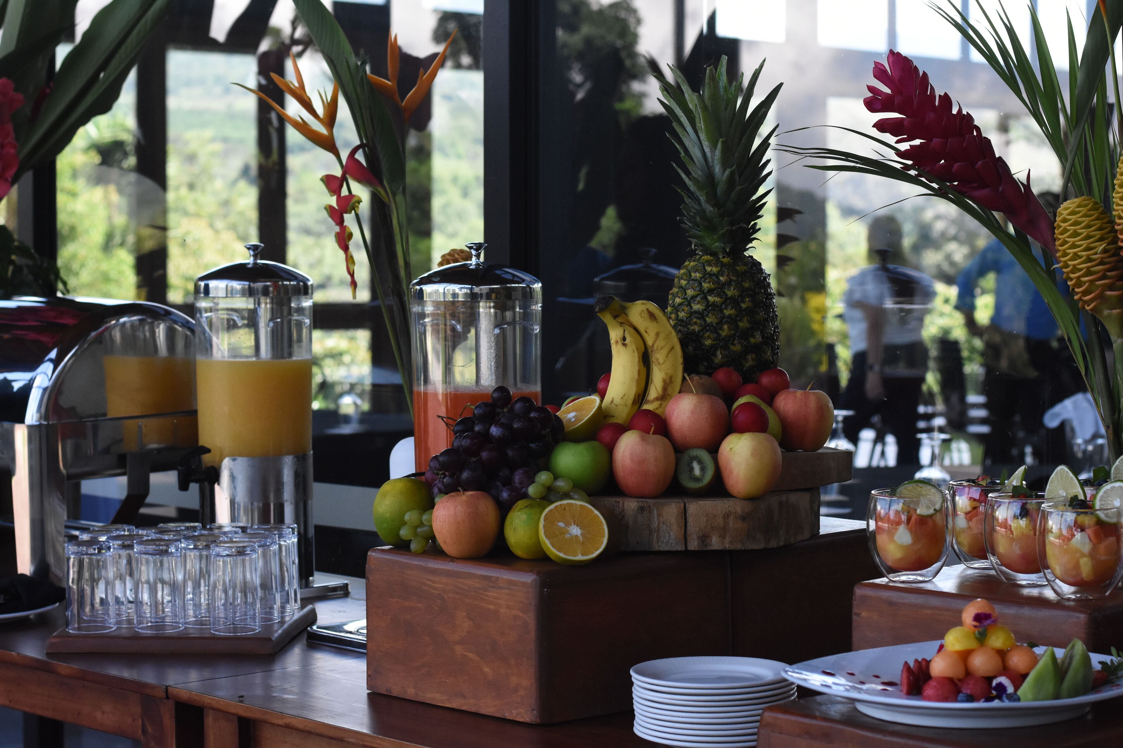 Un buffet de petit-déjeuner proposant des fruits, un coin pour se servir des jus de fruits et une vue sur l’extérieur.