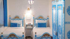 A room with two beds, each with a blue and white headboard, a bedside table with a lamp, and a wall-mounted light fixture.