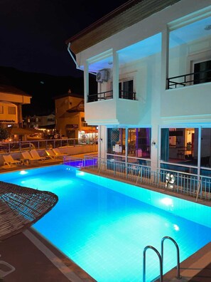 A swimming pool with a glass barrier and lounge chairs, surrounded by buildings with balconies and outdoor seating. - prestij apart otel (Marmaris)