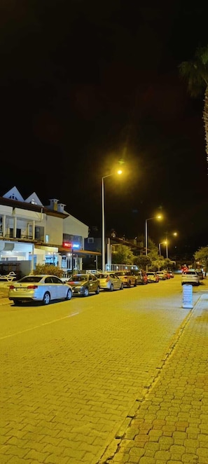 A nighttime street scene with parked cars, streetlights, and buildings with signage. - prestij apart otel (Marmaris)