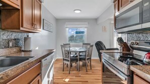 Una cocina moderna con armarios de madera, encimera de granito, una mesa de comedor con sillas y electrodomésticos de acero inoxidable.