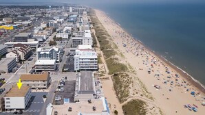 Vista aérea de uma cidade costeira com uma extensa praia, ladeada por edifícios e carros estacionados.