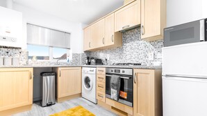 A modern kitchen with wooden cabinets, a washing machine, an oven, and a microwave. - Stunning 2-bed Apartment in Tipton Sleeps 3 (Tipton)