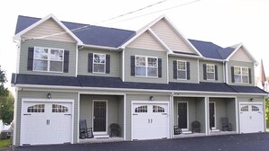 A two-story house with a front porch, two garages, and a symmetrical design. - Three Schooners Landing - Middle Condo (Sodus Point)