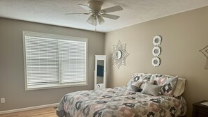 A bedroom with a bed, a ceiling fan, a window with blinds, a dresser, and wall decor. - Three Schooners Landing - Middle Condo (Sodus Point)