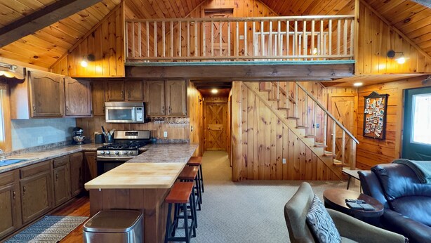 Eine großzügige Loft-Küche mit Holzwänden und einer Erkergalerie, ausgestattet mit einer Kochinsel, Barhocker und einer Treppe zum oberen Bereich.