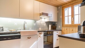 A modern kitchen with white cabinets, a stainless steel range hood, and a window with wooden shutters.