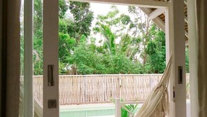 Una hamaca colgada de una estructura de techo de madera, con vista a una piscina y abundante vegetación.