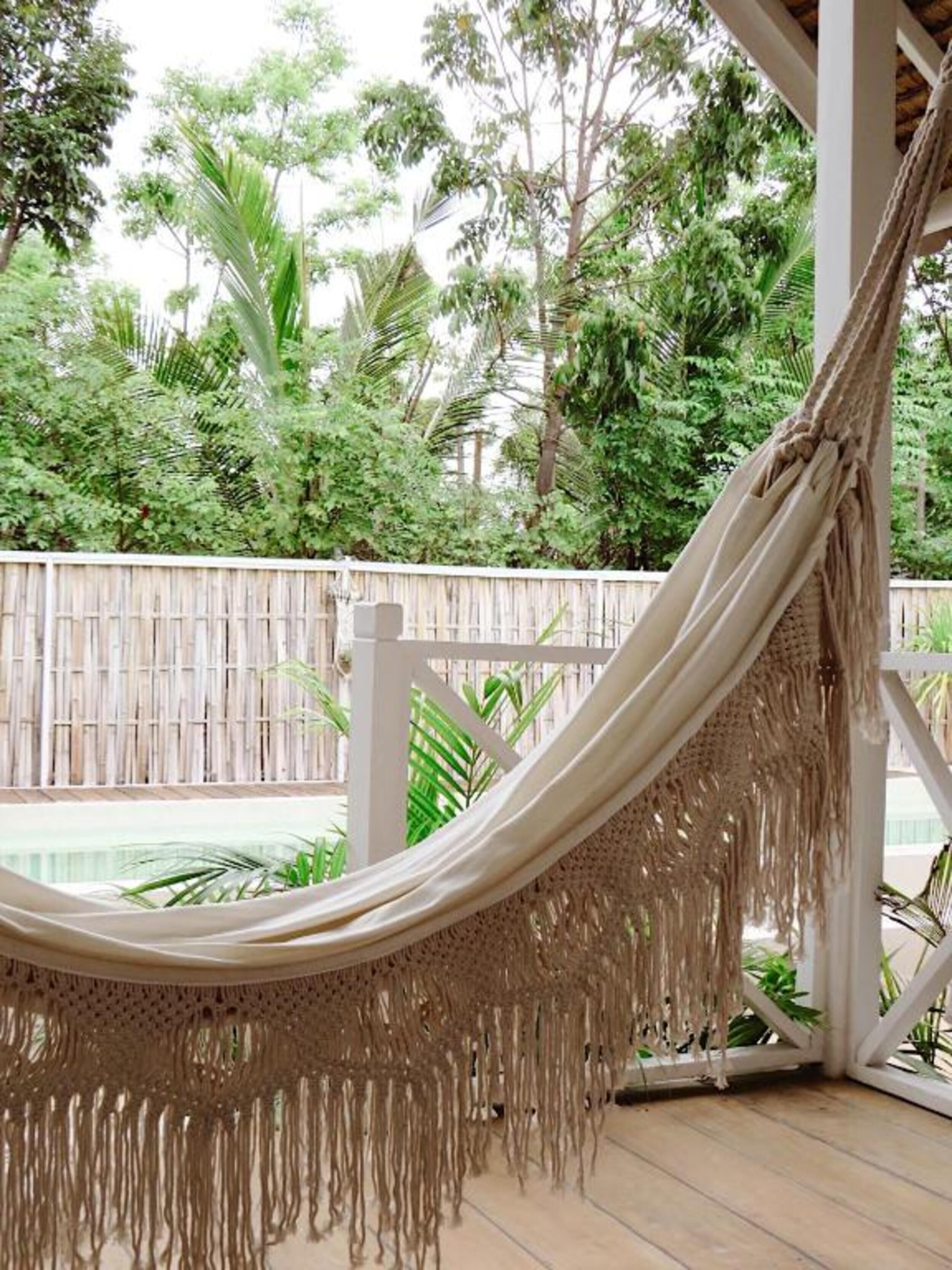 Un'amaca in una zona esterna riparata, con una piscina e vegetazione lussureggiante sullo sfondo.