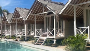 Una hilera de bungalows sobre el agua con techos de paja, una piscina y palmeras.