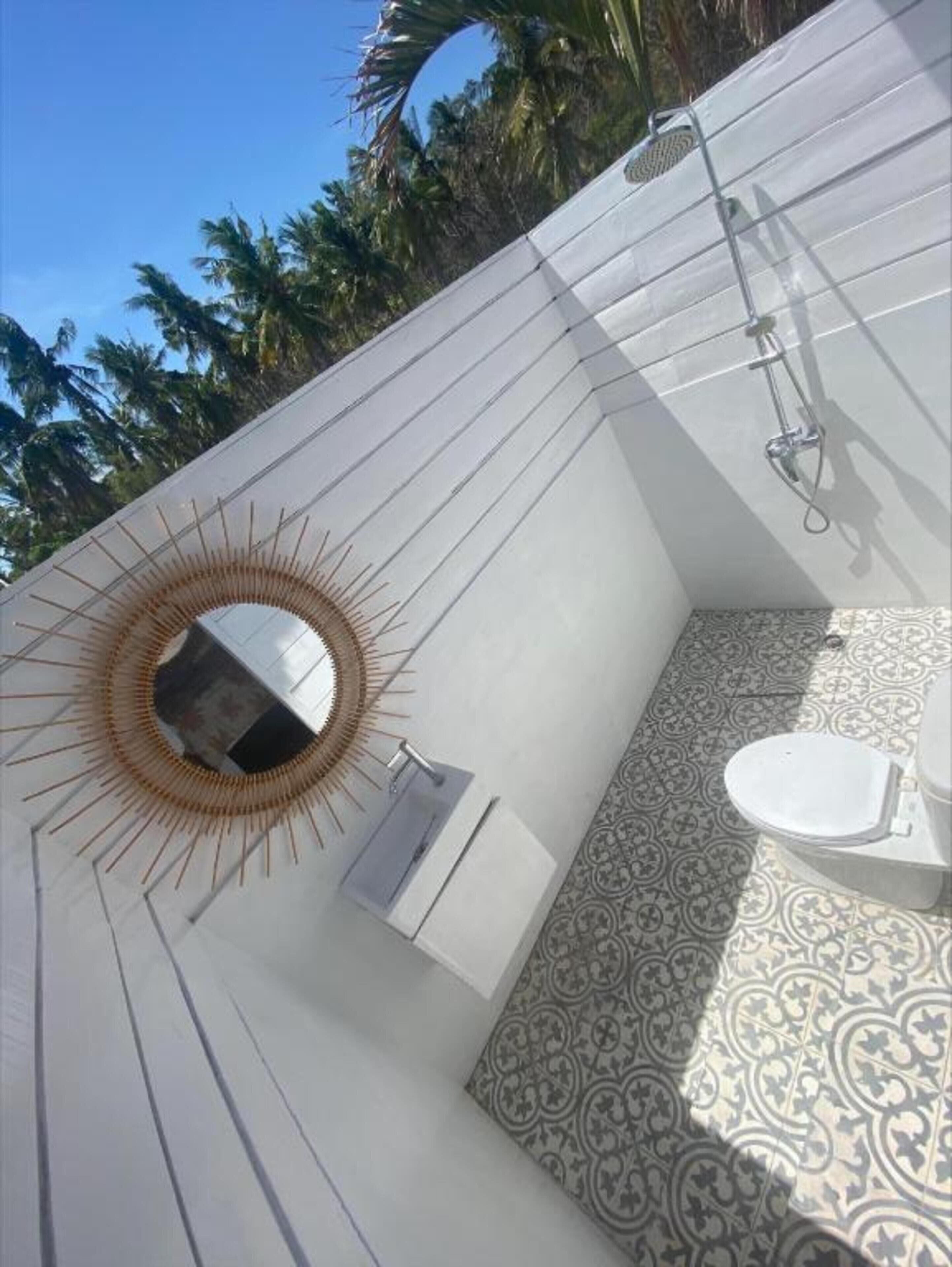 A bathroom with a curved ceiling, a sunburst mirror, a toilet, and patterned tiles.