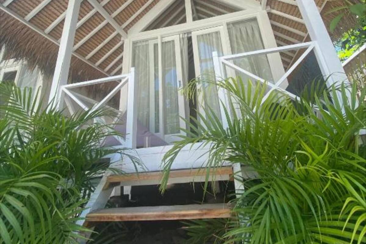 Una construcción con techo de paja y una escalera de madera que conduce a una puerta de cristal.
