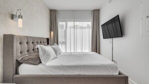 A modern bedroom with a large bed, a flat-screen TV, and a wall-mounted light fixture. - Initial Ilot Downtown Québec (Québec City)