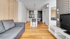 A modern living room with a grey sofa, a TV on a white stand, and a kitchen in the background. - Initial Ilot Downtown Québec (Québec City)