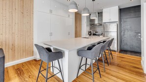 A modern kitchen with white cabinets, a large island with bar stools, pendant lighting, and a stainless steel refrigerator. - Initial Ilot Downtown Québec (Québec City)