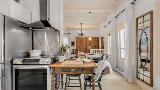 A modern kitchen with stainless steel appliances, a wooden dining table, and a chandelier. - Initial | La petite école | Île d'Orléans (Saint-Laurent-de-l'Île-d'Orléans)