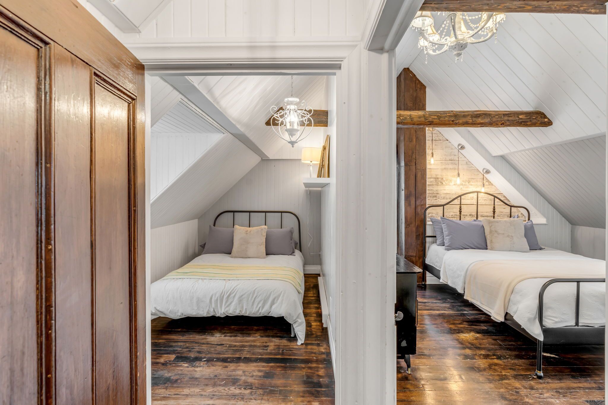 A bedroom with two beds, wooden beams, a chandelier, and a sloped ceiling.