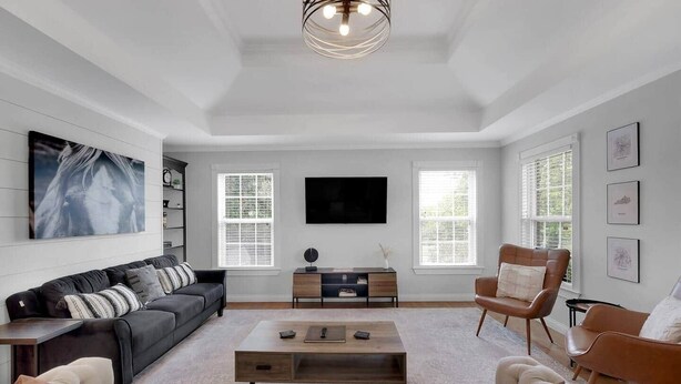 A spacious living room with a large flat-screen TV, a black leather sofa, a brown leather armchair, and a beige sofa.