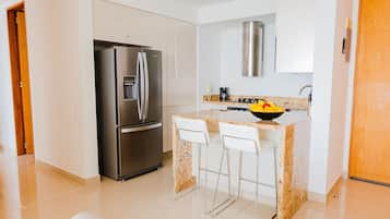 Uma cozinha moderna com geladeira de aço inoxidável, bancada de granito, banquetas brancas e forno embutido.