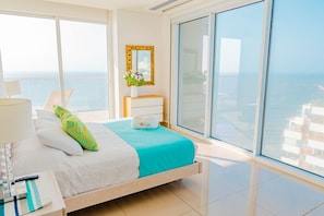 A hotel room with a bed, a bedside table with a lamp, a vase with flowers, and a view of the ocean. - U-GO Edificio H2 (Cartagena)