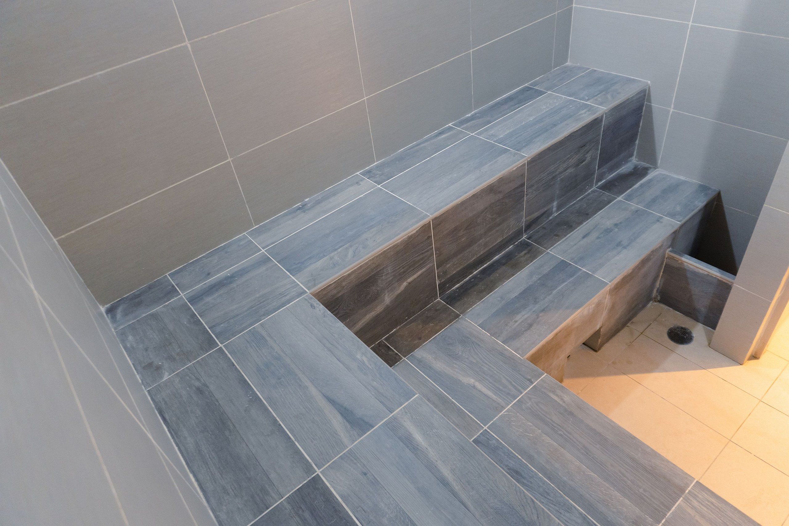 Un bagno con piastrelle grigie, una panca integrata e uno spazio doccia.