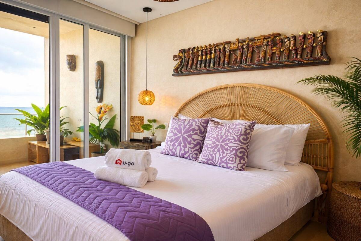 Habitación de hotel con cama, ventana grande, una obra de arte en la pared y balcón con plantas.