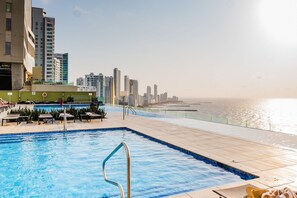 Piscina con escalera metálica, sillas de descanso y vista al mar y al horizonte de la ciudad.