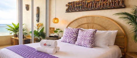 A hotel room with a bed, a large window, a wall art piece, and a balcony with plants.