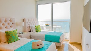 Une chambre d’hôtel avec deux lits, un balcon donnant sur la mer, une télévision et un chapeau de la marque U-go posé sur l’un des lits.