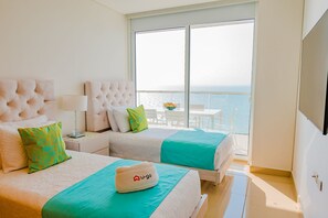 Une chambre d’hôtel avec deux lits, un balcon donnant sur la mer, une télévision et un chapeau de la marque U-go posé sur l’un des lits.