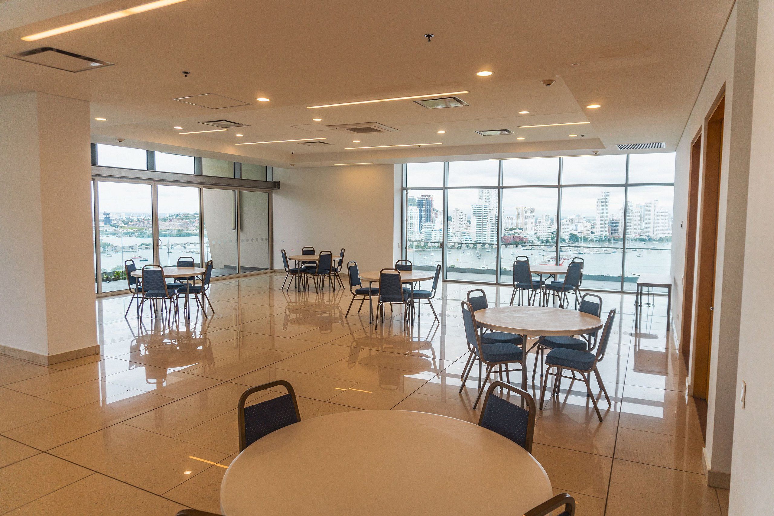 A spacious conference room with large windows, multiple tables, and chairs arranged for meetings.