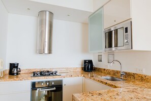 A modern kitchen with stainless steel appliances, a granite countertop, and white cabinetry. - U-GO Edificio H2 (Cartagena)