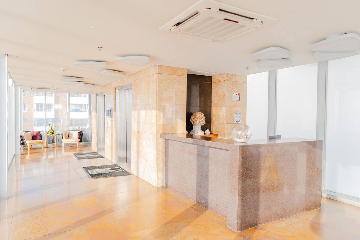 Un espace d’accueil doté d’un comptoir en marbre, d’un petit coin salon avec un canapé et une table, et offrant une vue sur l’extérieur grâce à de grandes fenêtres.