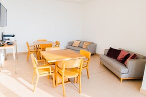 Ein modernes Wohnzimmer mit einem Holzesstisch, Stühlen, einem grauen Sofa und einem an der Wand befestigten Fernseher.