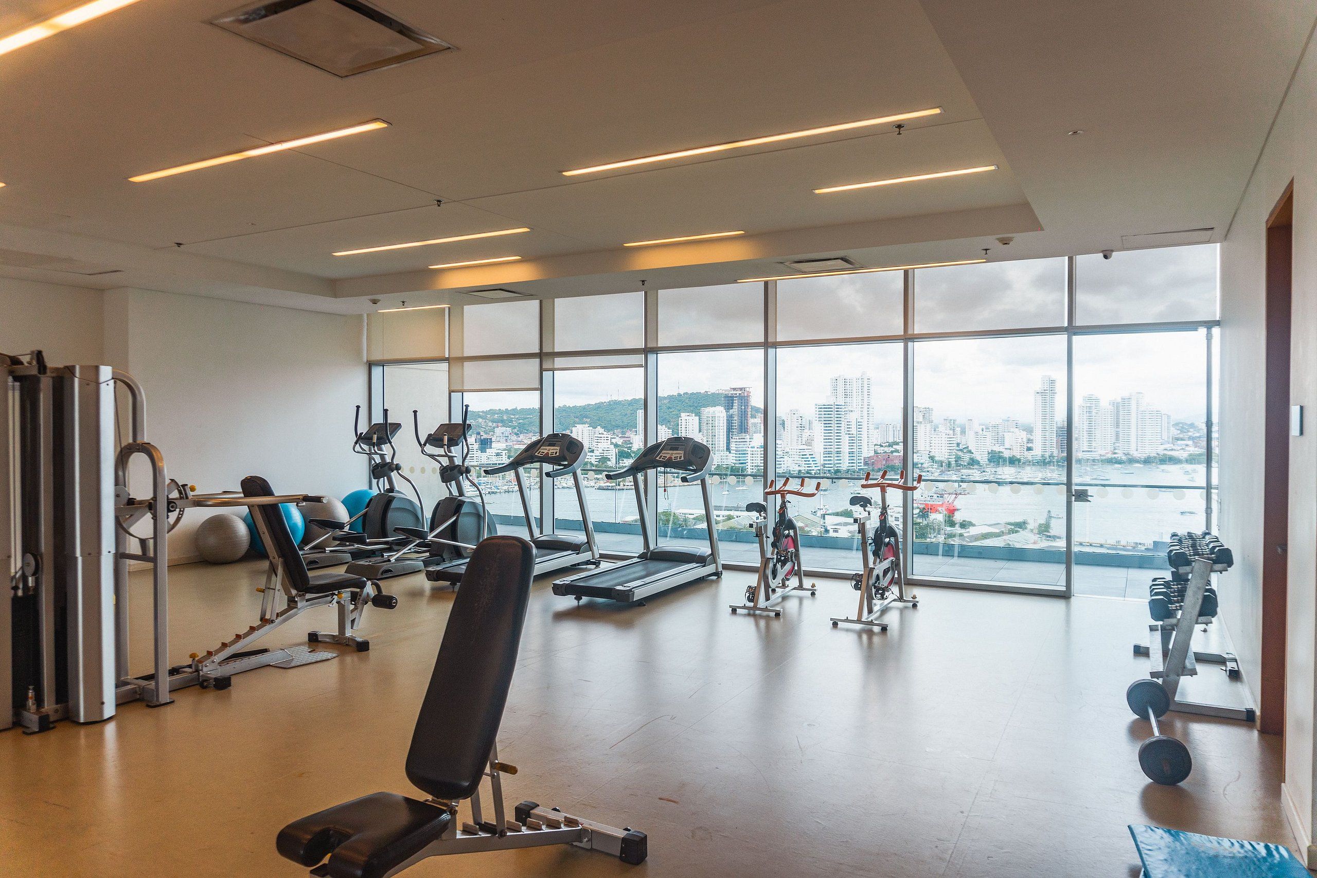 A gym with exercise equipment, large windows, and a view of a cityscape.