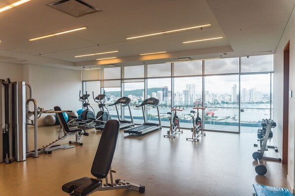 A gym with exercise equipment, large windows, and a view of a cityscape.