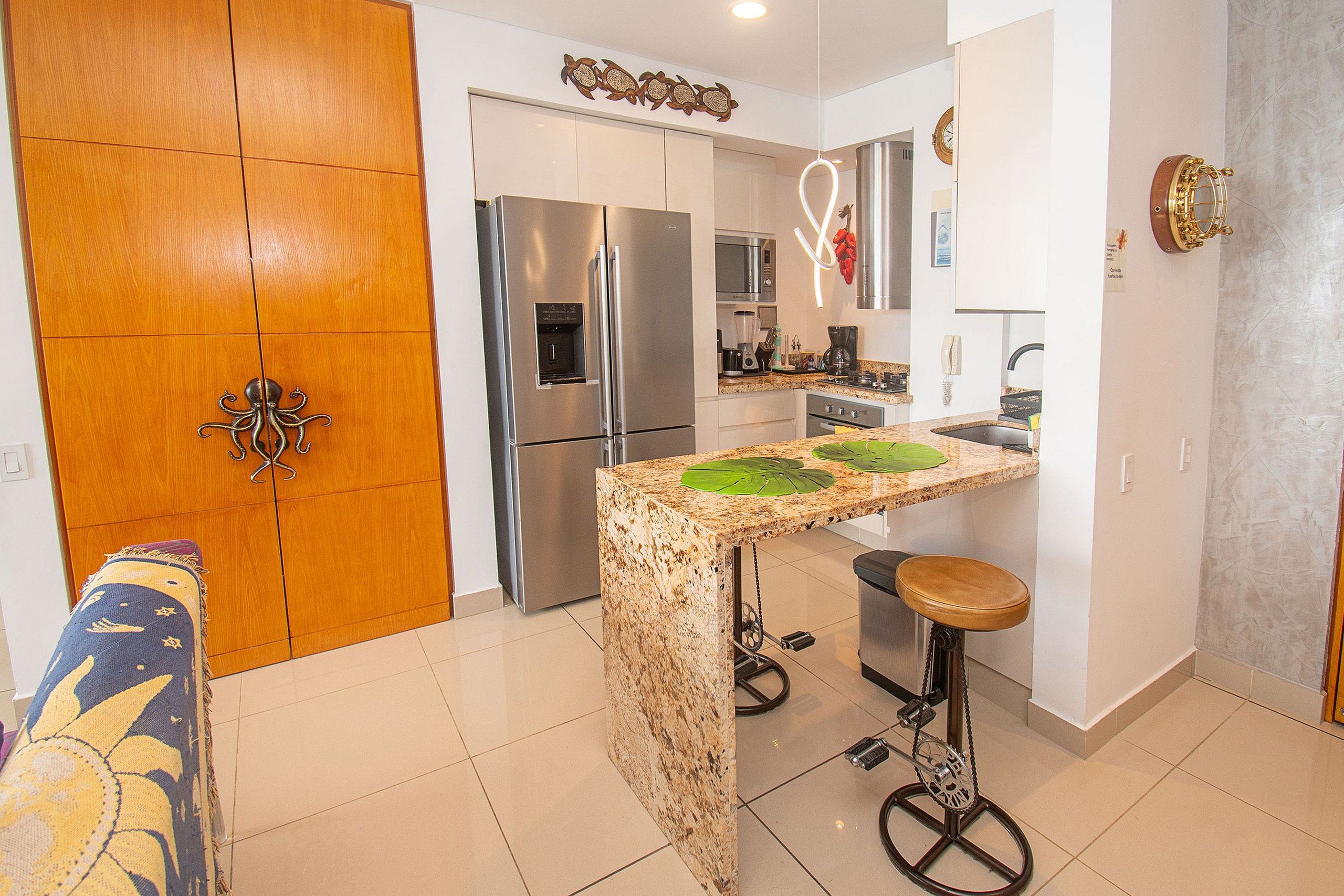 Una cucina compatta con isola centrale, elettrodomestici in acciaio inossidabile e una porta in legno con maniglia decorativa.