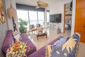 Uma sala de estar espaçosa com uma televisão grande, assentos confortáveis e vista para a cidade.