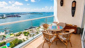 Un balcon avec des fauteuils en osier, une table ronde et une vue sur un port où sont amarrés des bateaux.