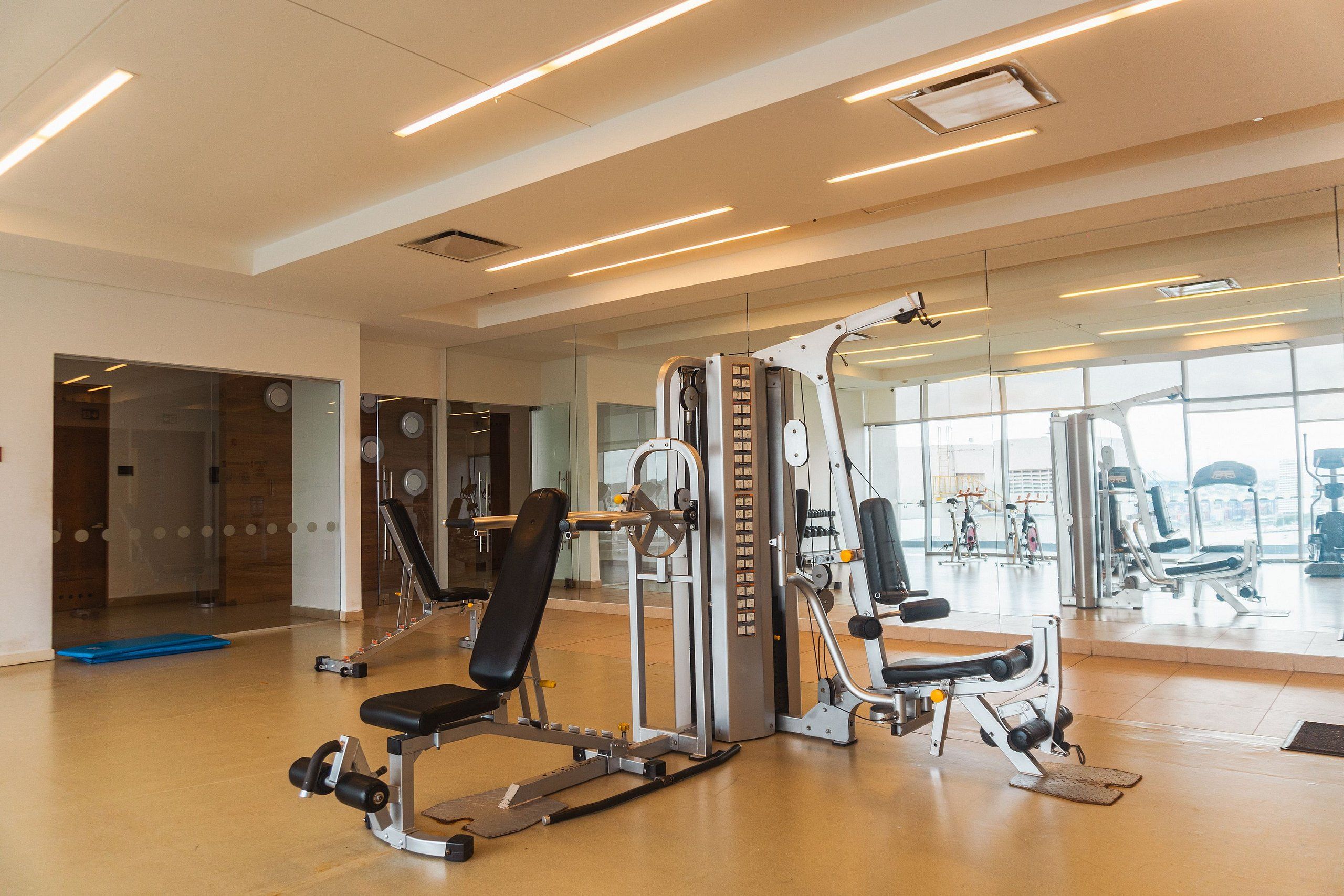 A gym with exercise machines, a blue mat, and large windows.
