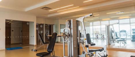 A gym with exercise machines, a blue mat, and large windows.