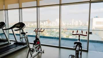 Academia com esteiras e bicicletas ergométricas, janelas amplas com vista para a cidade.
