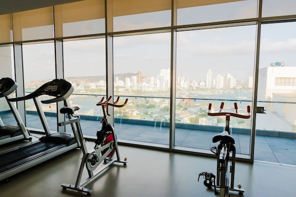 A gym with treadmills and stationary bikes, large windows with a city view.