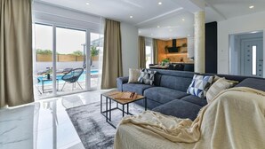 A modern living room with a sofa, a coffee table, and a view of an outdoor pool area. - Holiday Home in Bibinje with Seaview, Balcony, Air condition, WIFI (5201-1) (Bibinje)