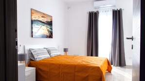 A bedroom with a bed, a nightstand, a lamp, a painting, and curtains. - Seaside Serenity - Luxe Penthouse - near the beach (Il-Mellieha)
