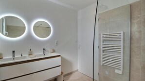 A modern bathroom with a white vanity, two round mirrors with underglow lighting, a glass shower enclosure, and a white towel rack. - Maison 6 Personnes, SPA (Penmarc'h)